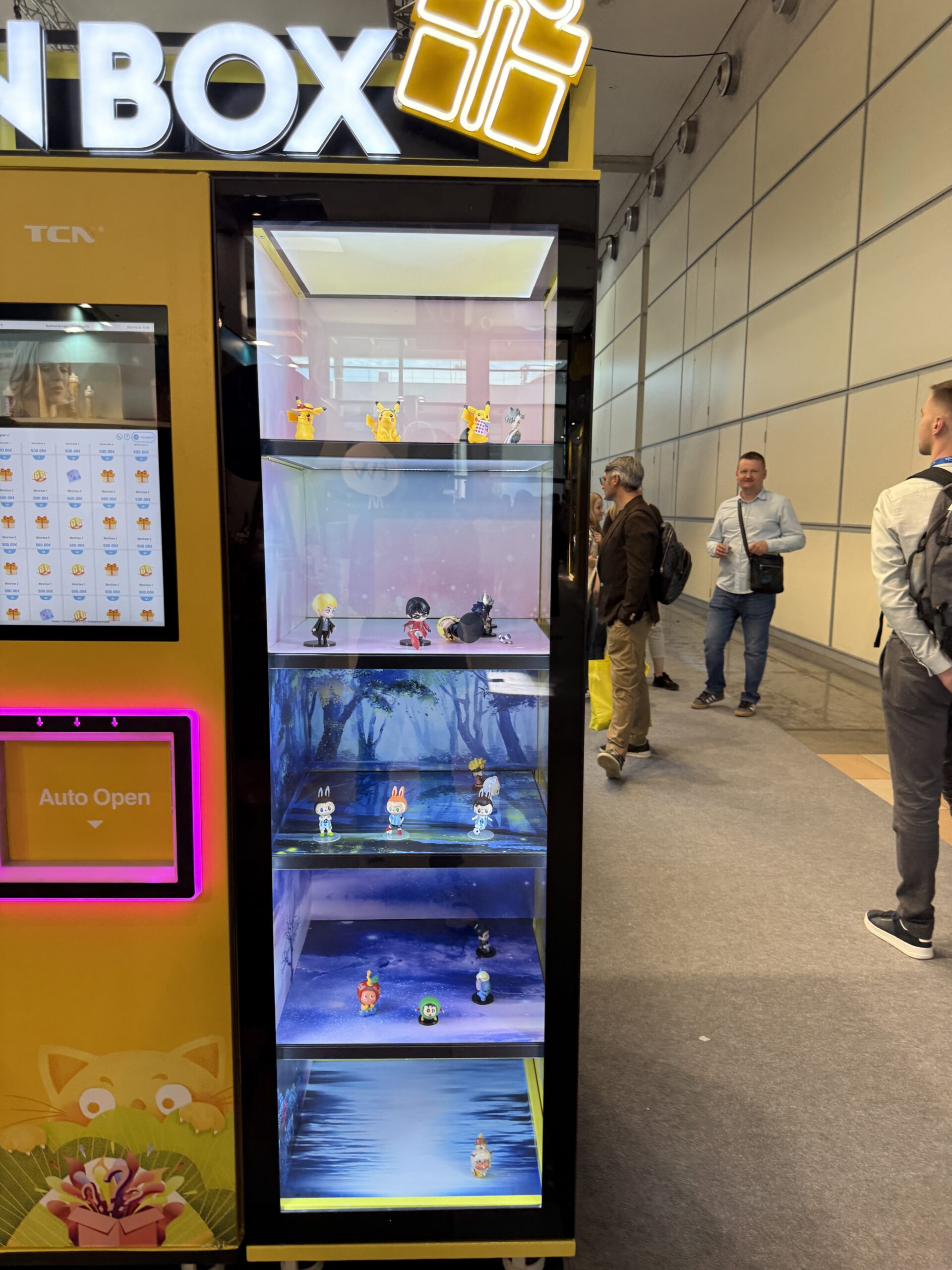 Large vertical touchscreen with product tiles on a trading card vending machine, usable as advertising space